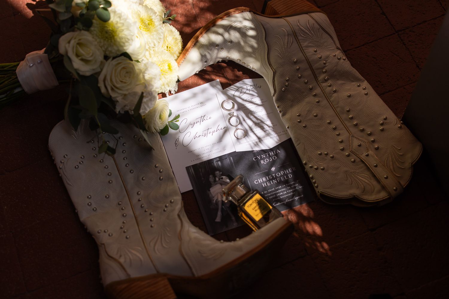 Wedding bouquet of white roses beside rings and ceremony program on a white lace surface.