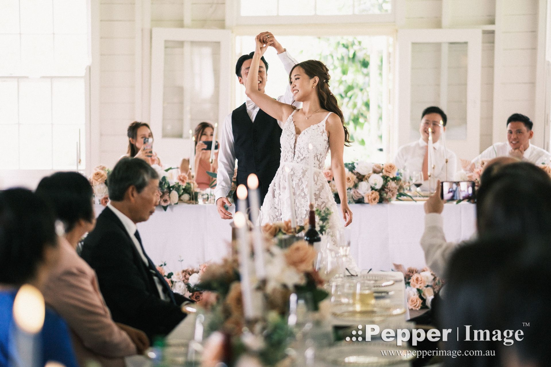 Bride and groom share a romantic dance at elegant wedding reception with guests seated at floral-decorated tables.
