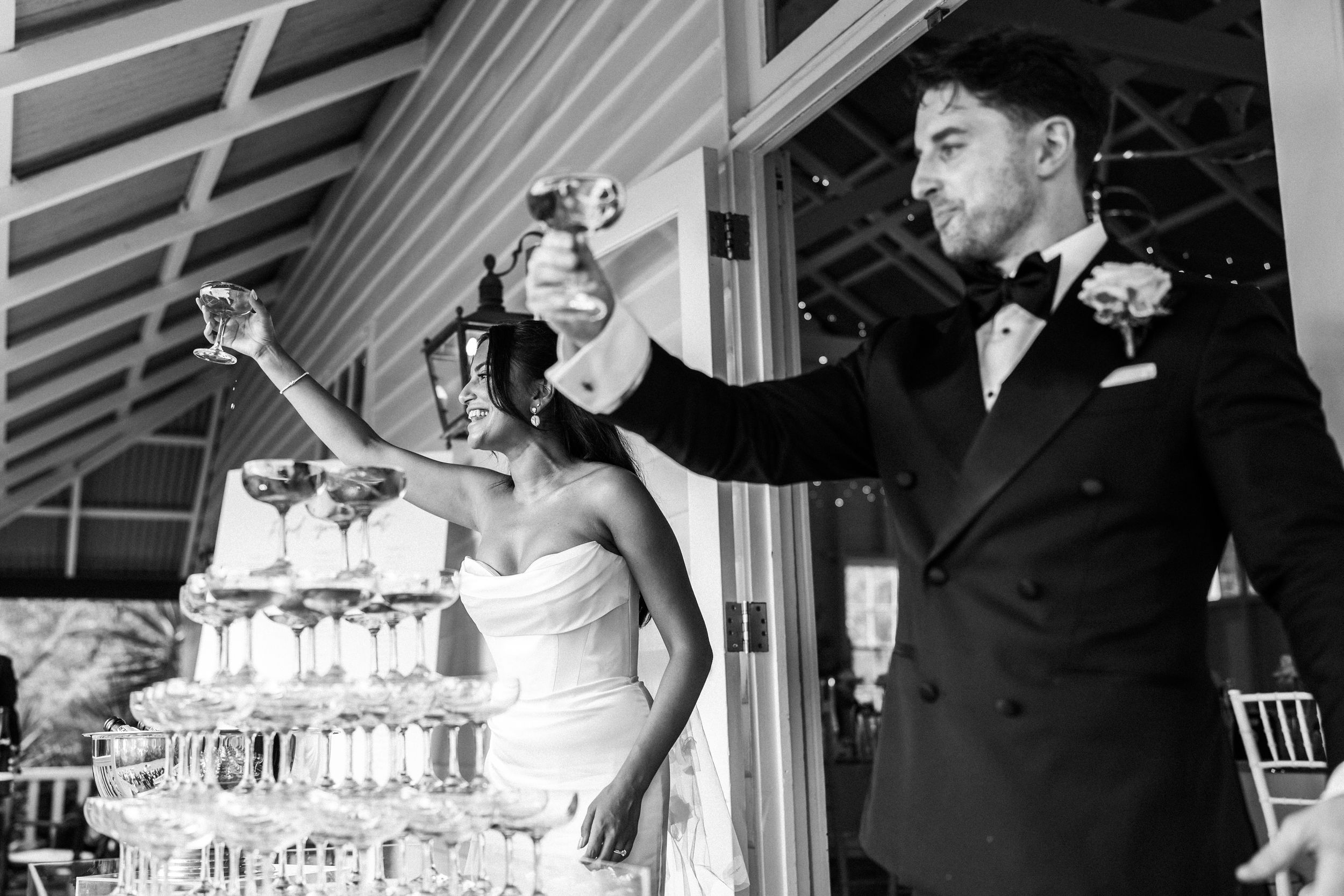 Bride and groom pouring champagne tower at elegant wedding reception in black and white photo.