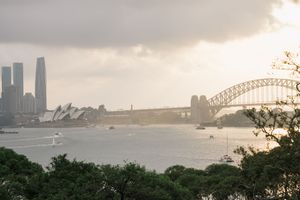 Sydney Harbour panorama featuring the Opera House, Harbour Bridge, and boats on the water under a dramatic cloudy sky.