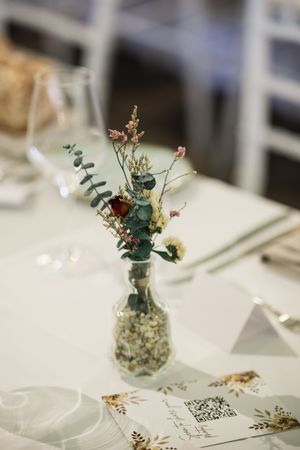 Elegant table setting with a small glass vase of dried wildflowers and eucalyptus, beside a menu card with QR code.