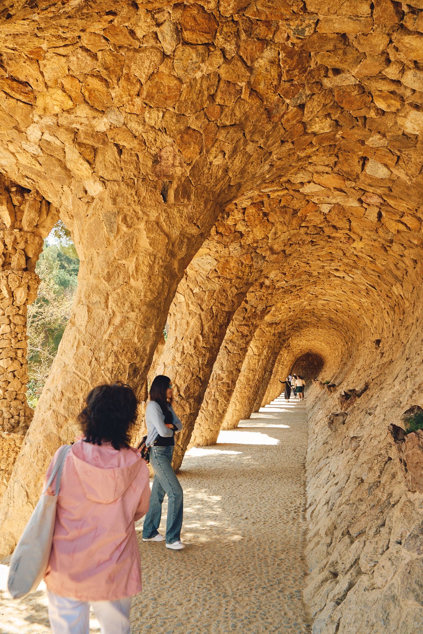 Tourists walking through the iconic stone colonnade corridor at Park Güell, Barcelona, designed by Antoni Gaudí.