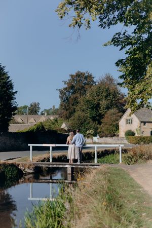 Couple standing on a small bridge over a stream in a picturesque Lower Slaughter village on a sunny day.