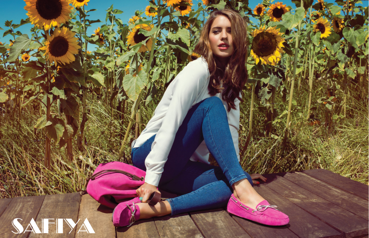 Woman in pink loafers sitting by sunflowers in jeans for Safiya footwear campaign.