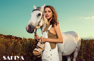 Model in white overalls holding white horse in sunflower field for Safiya shoes.