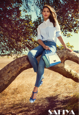 Woman in white shirt and jeans with blue bag in tree for Safiya fashion campaign.