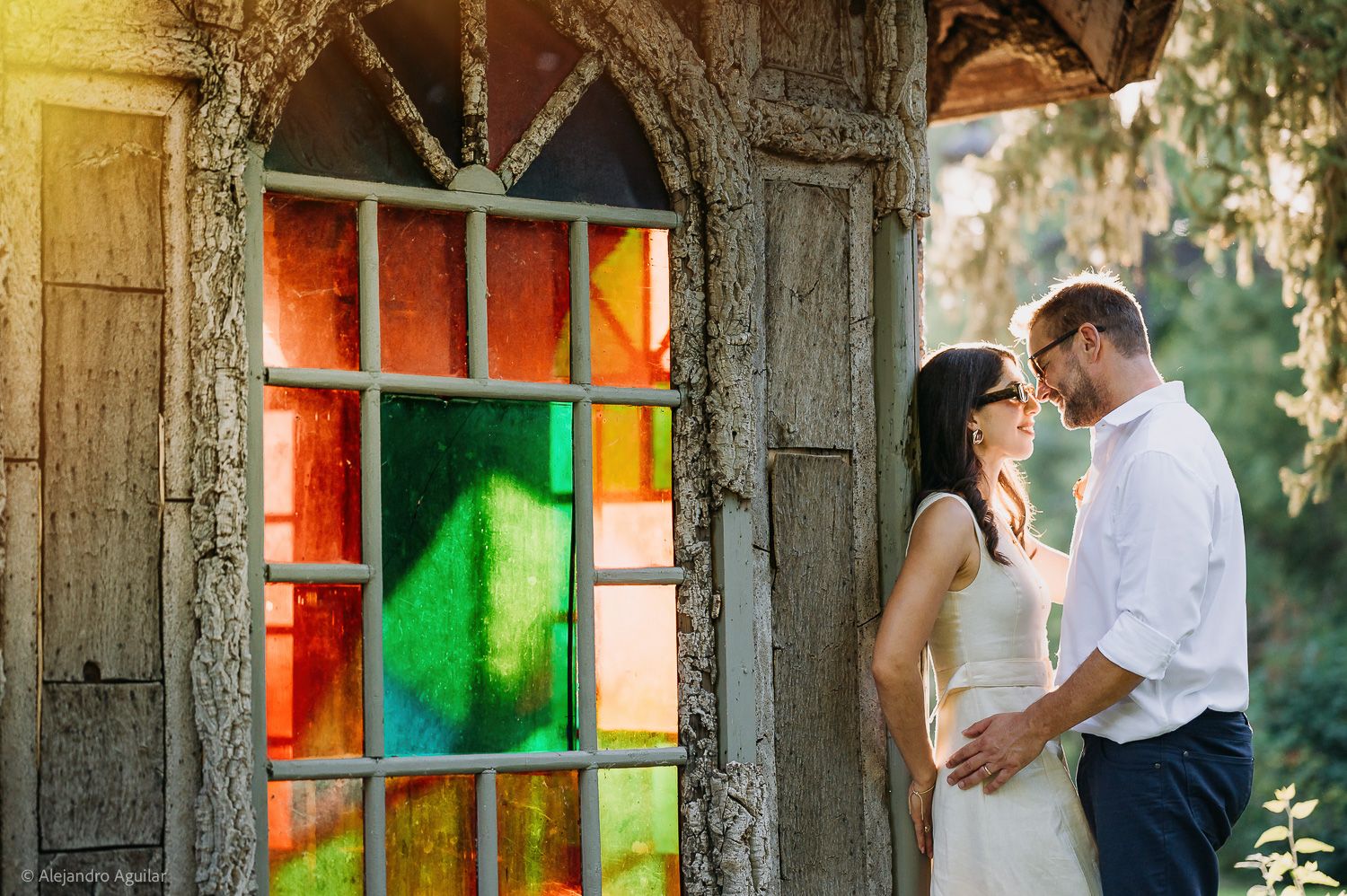 Couple sharing a romantic moment beside a colorful stained glass window on their wedding day.