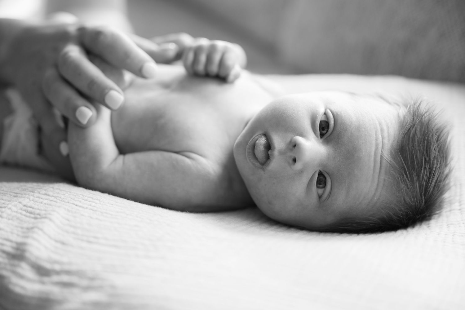 a black and white of newborn baby with eyes open and sticking tongue out during in-home lifestyle newborn session in Minnetonka/Hopkins, MN.