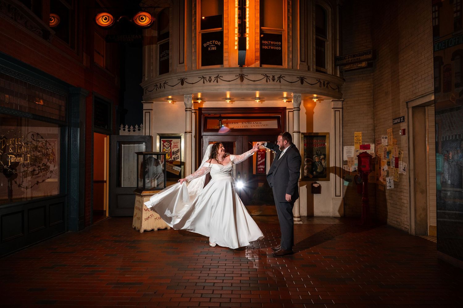 Bride and groom dancing outside a historic venue at night, bride's white gown flowing under warm lights.