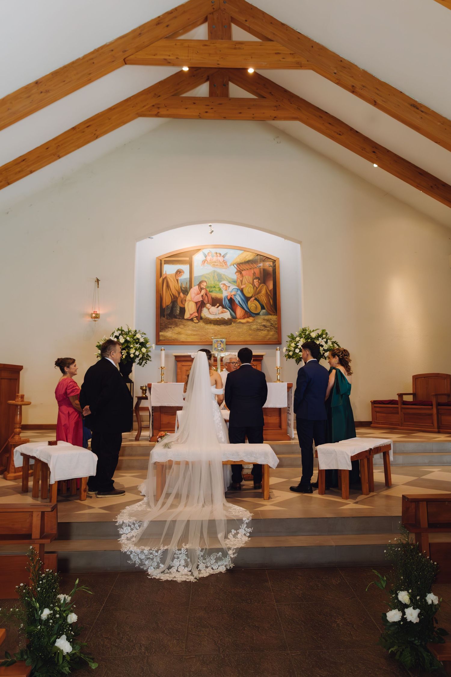 Bride and groom exchange vows at the altar of a small white chapel with wooden beam ceiling and nativity painting.