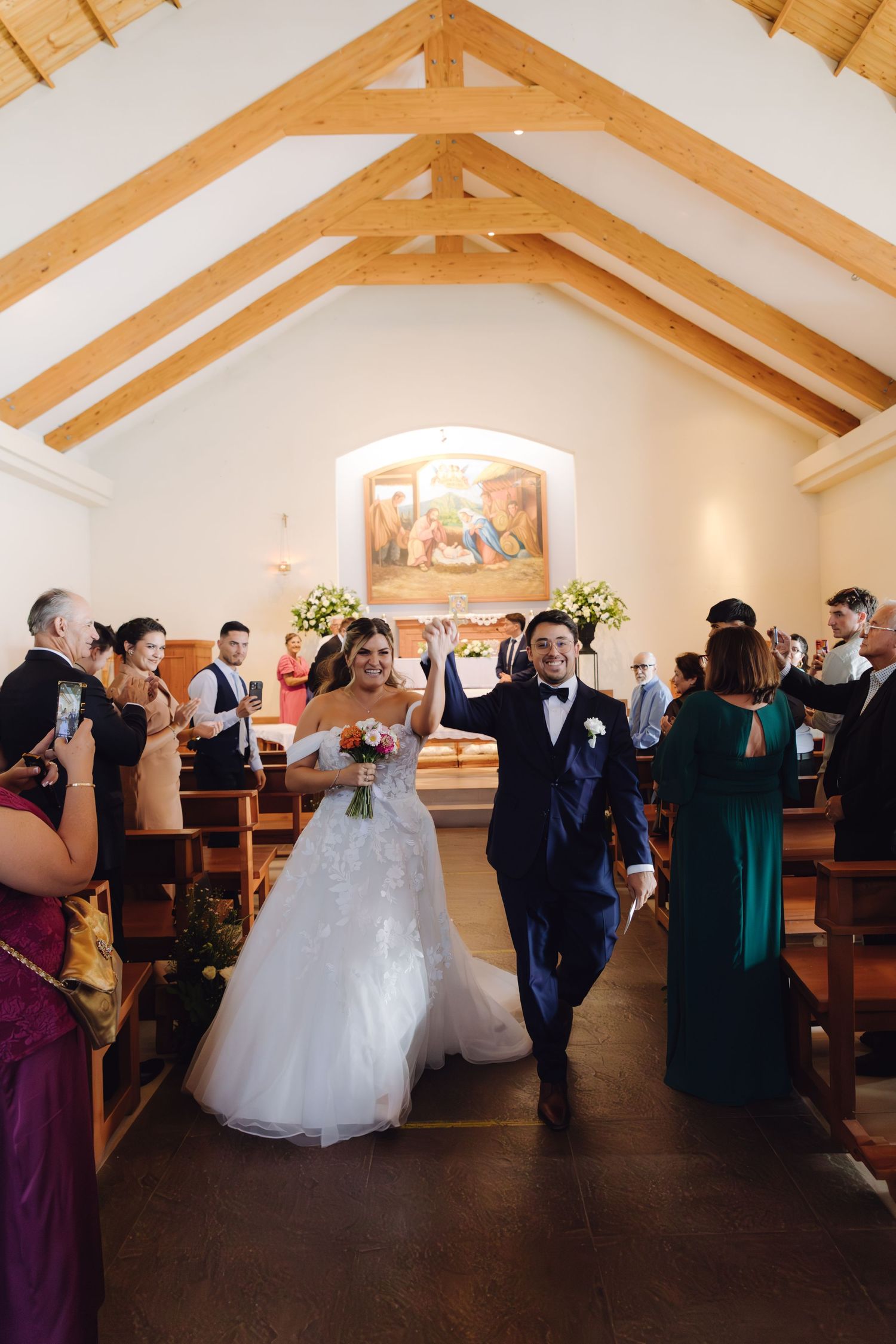 Newlyweds celebrate joyfully walking down the aisle after their wedding ceremony in a charming white chapel.