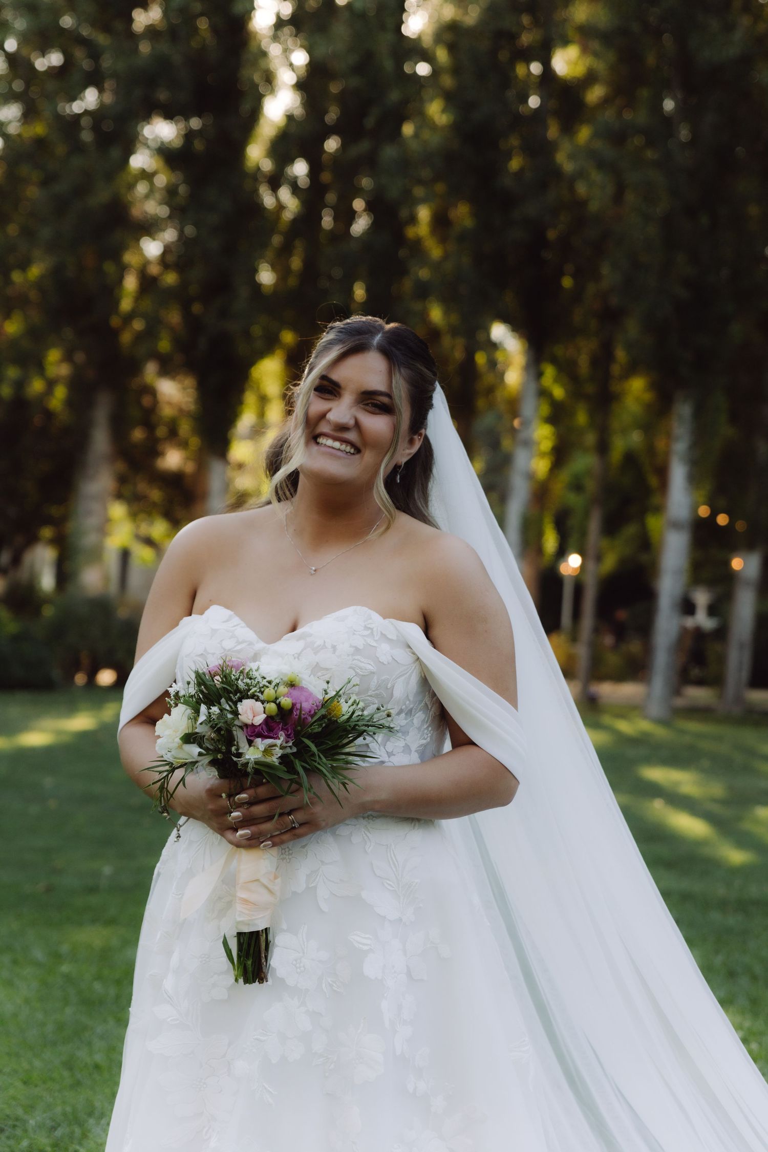 Radiant bride in strapless lace wedding dress laughing while holding a colorful floral bouquet.