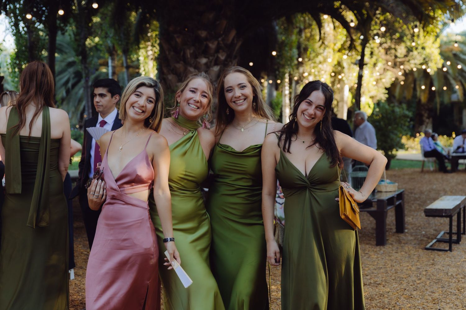 Four bridesmaids in satin green and pink dresses posing together at outdoor wedding reception.