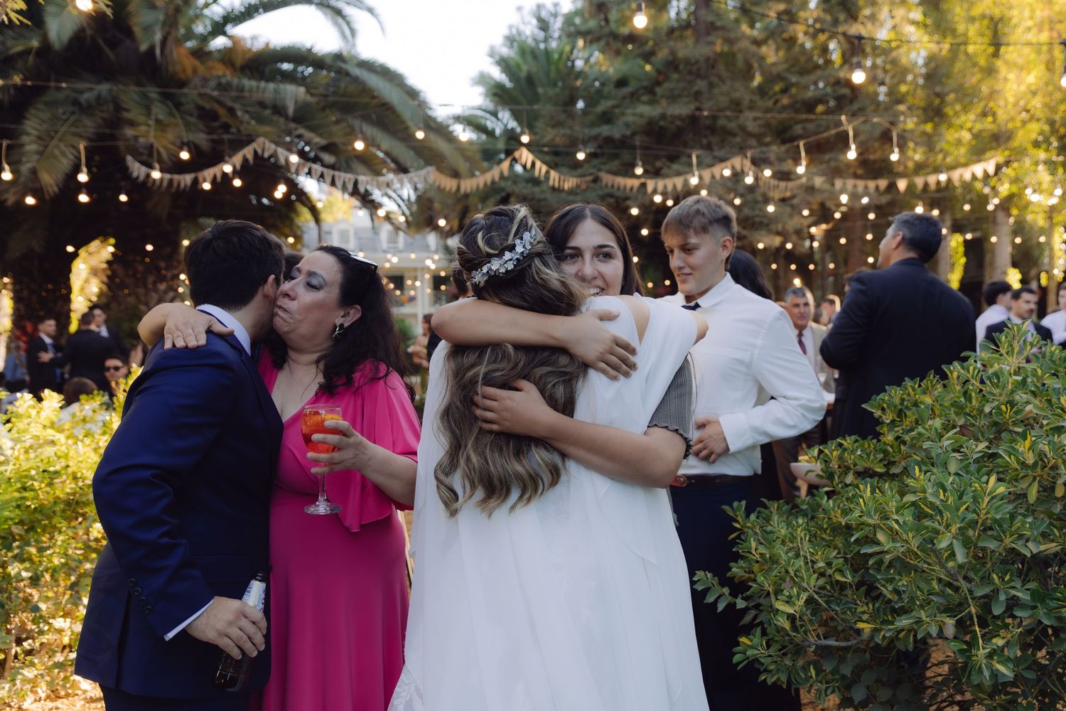 Bride and groom embracing wedding guests outdoors under string lights at an elegant garden reception.