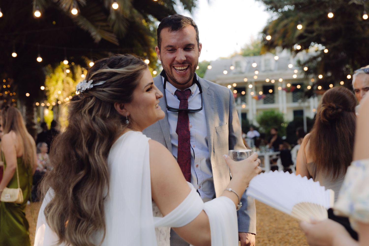 Bride and groom laughing joyfully with guests at an elegant outdoor wedding reception at dusk.