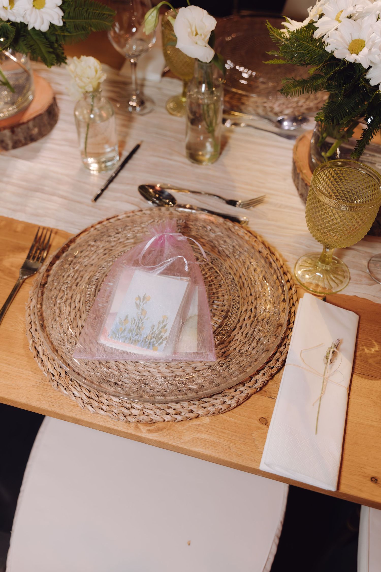 Rustic woven charger plate with pink gift bag favor on wooden wedding reception table.