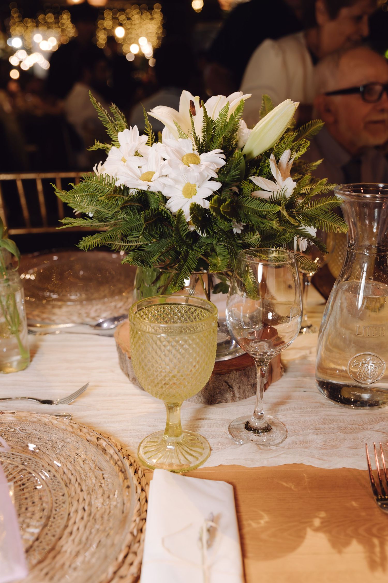 Beautiful white daisy and lily floral centerpiece in green vase on elegantly set wedding table.