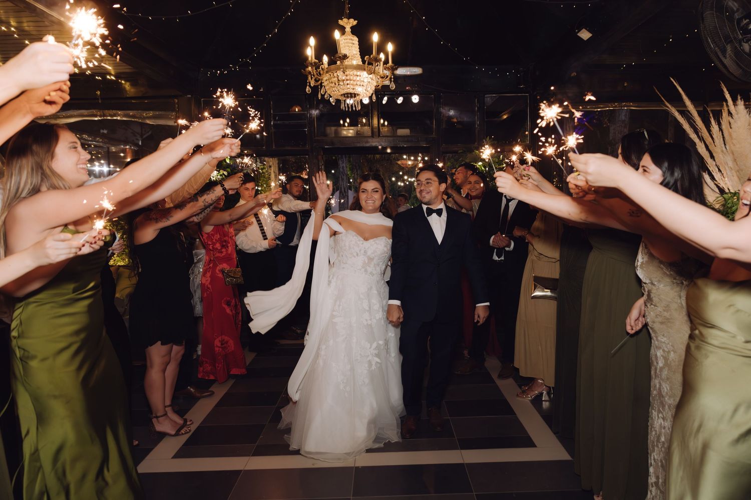 Newlyweds walk through a glowing sparkler tunnel surrounded by guests at their wedding reception exit.