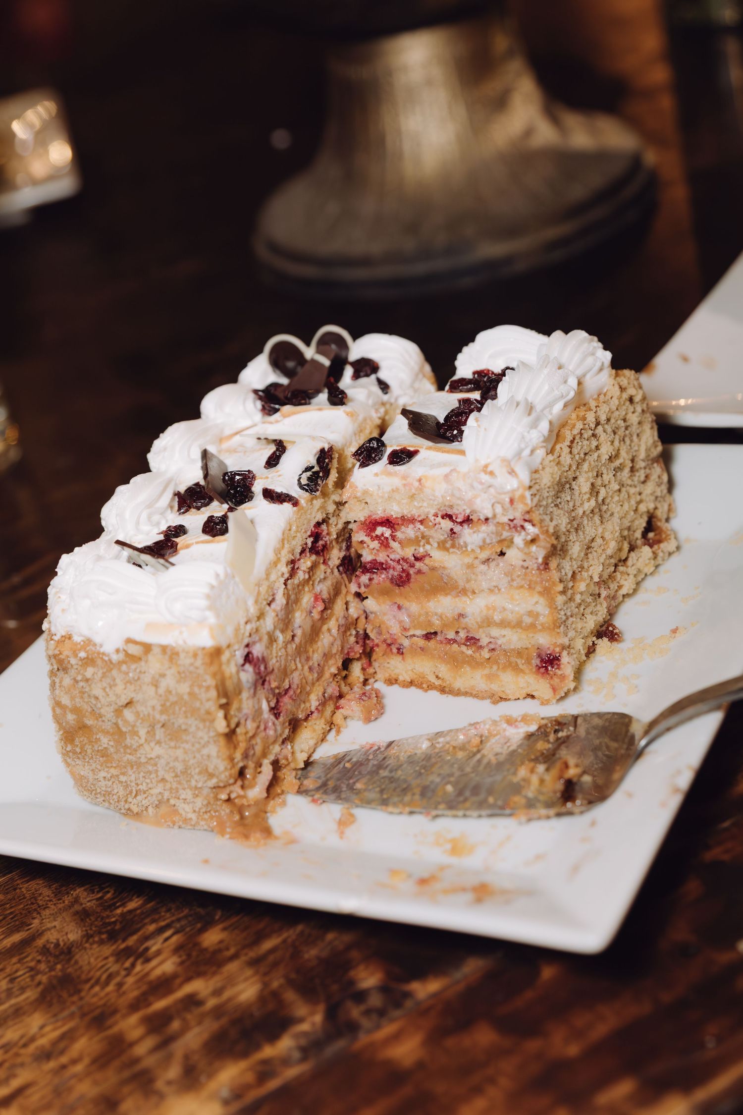 Slice of layered wedding cake with white frosting, berry filling, and chocolate shavings on white plate.
