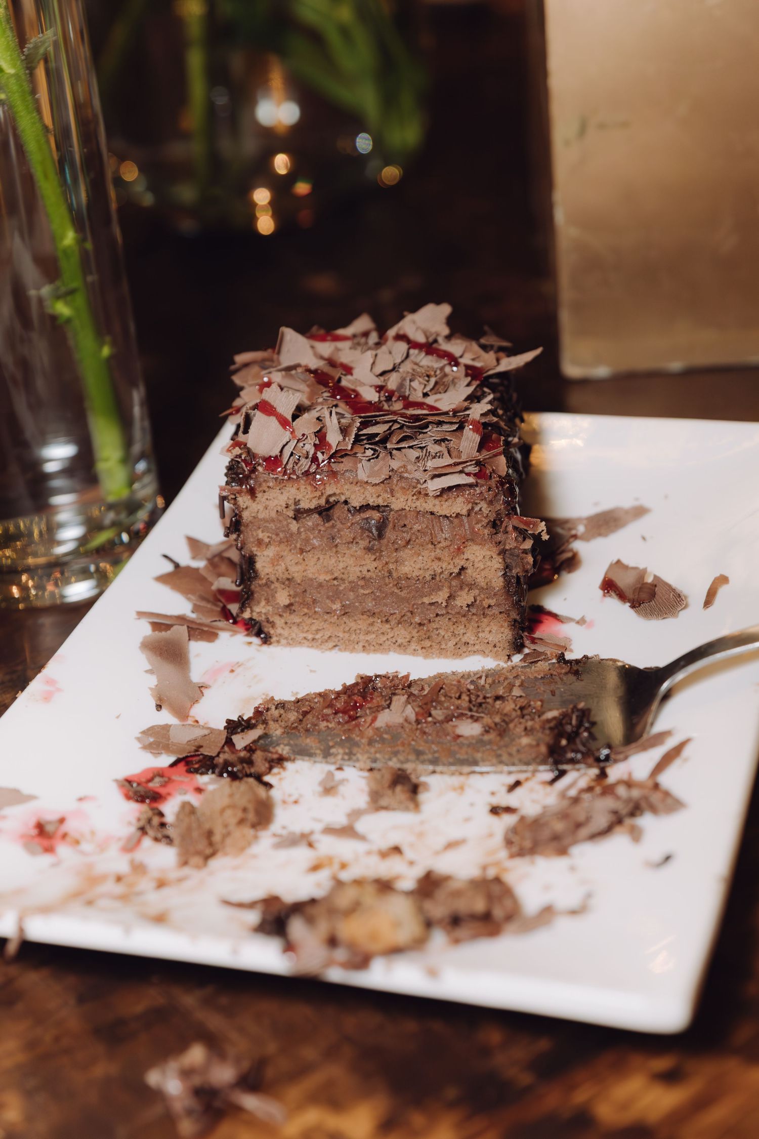 Elegant slice of chocolate layer cake with red berry filling and chocolate shavings on white plate.