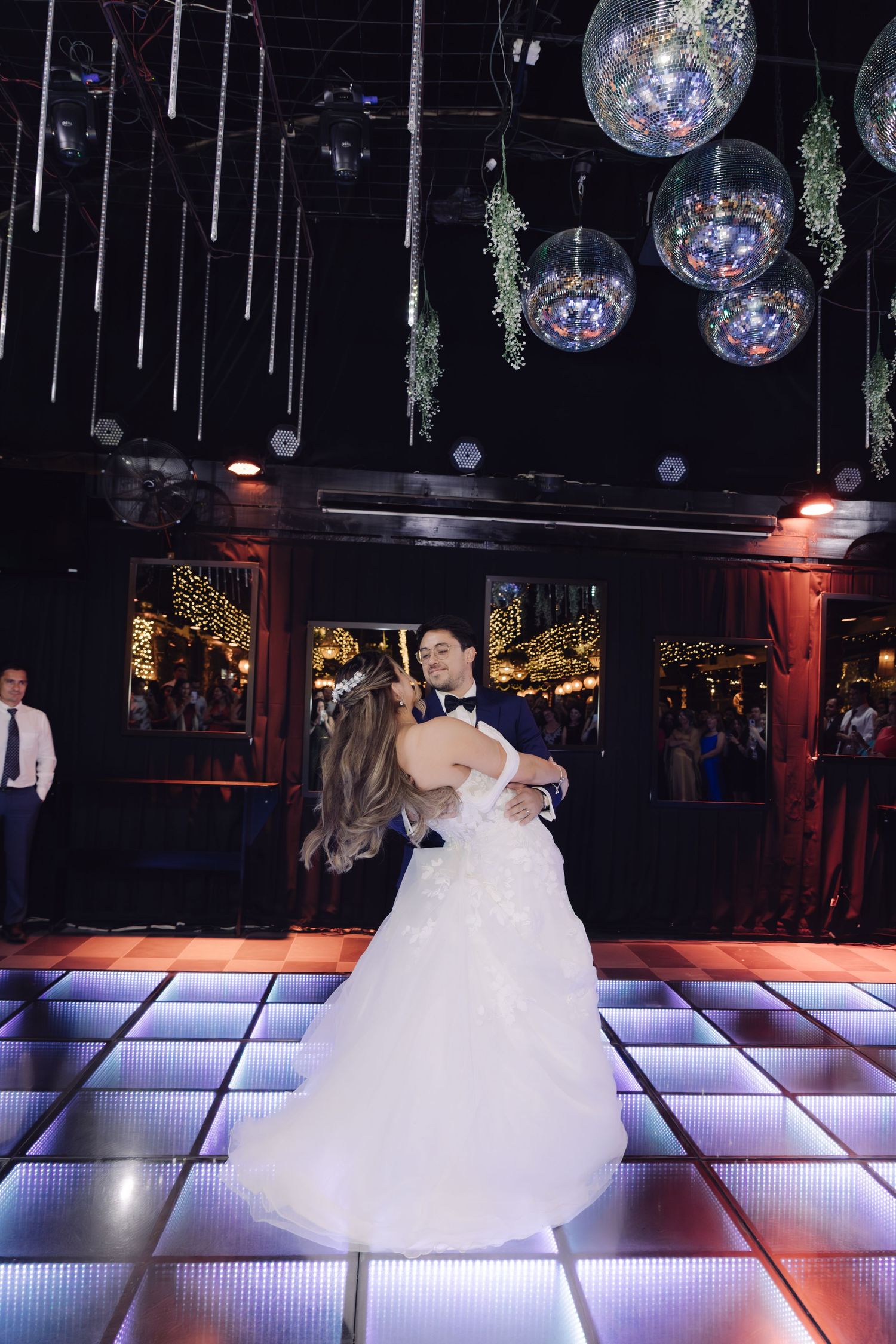 Bride and groom share their first dance under sparkling disco ball ceiling at wedding reception venue.