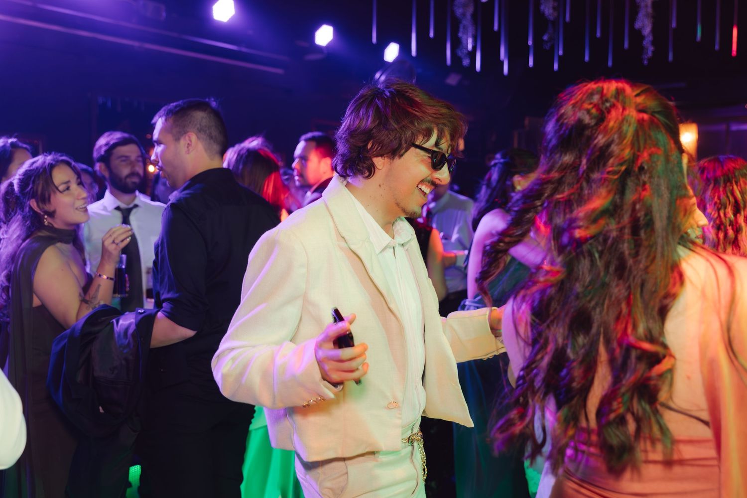Stylish guest in white suit and sunglasses dancing at an elegant evening wedding reception party.