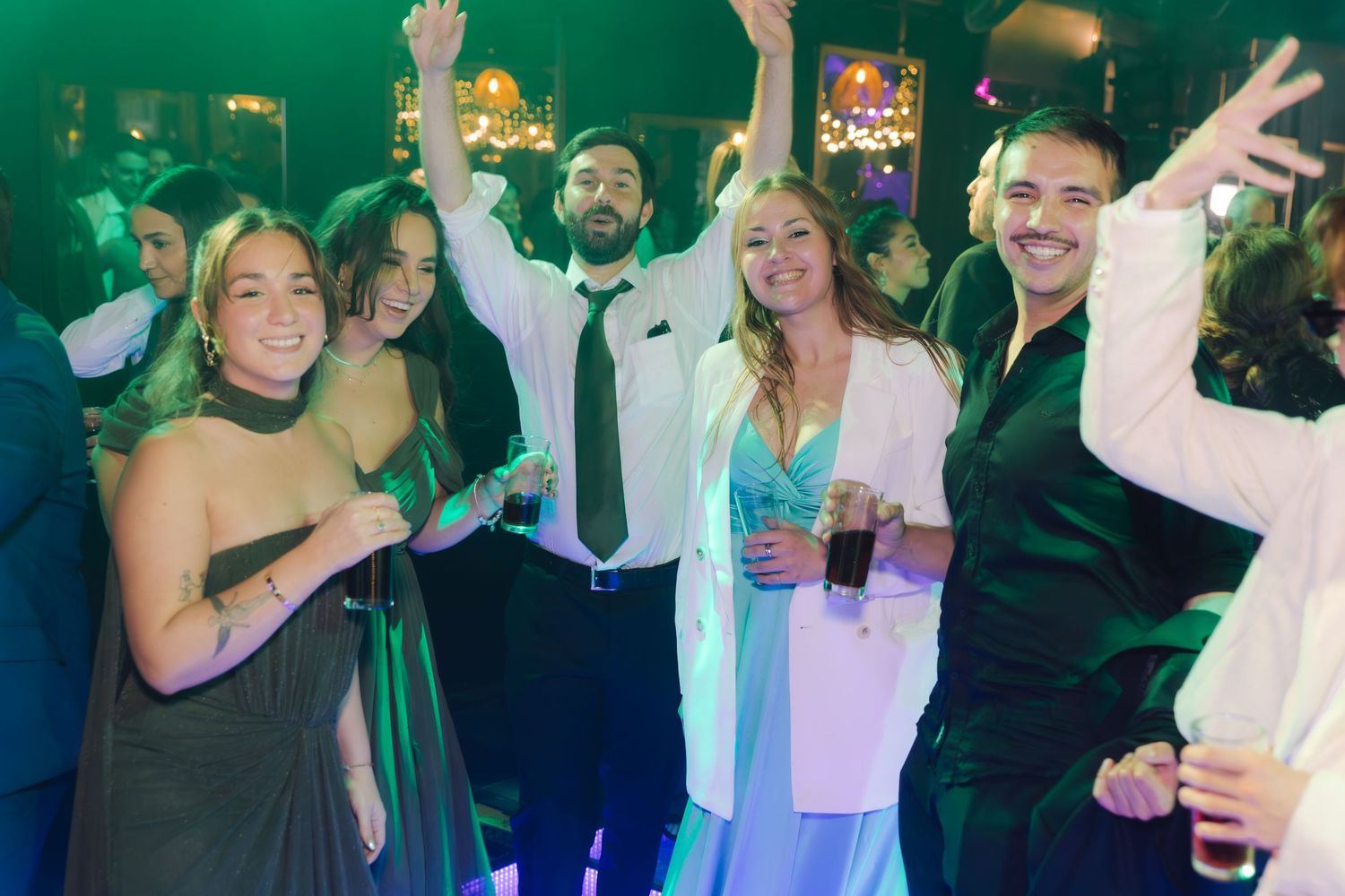 Happy wedding guests posing and dancing together under colorful lights at a festive reception celebration.