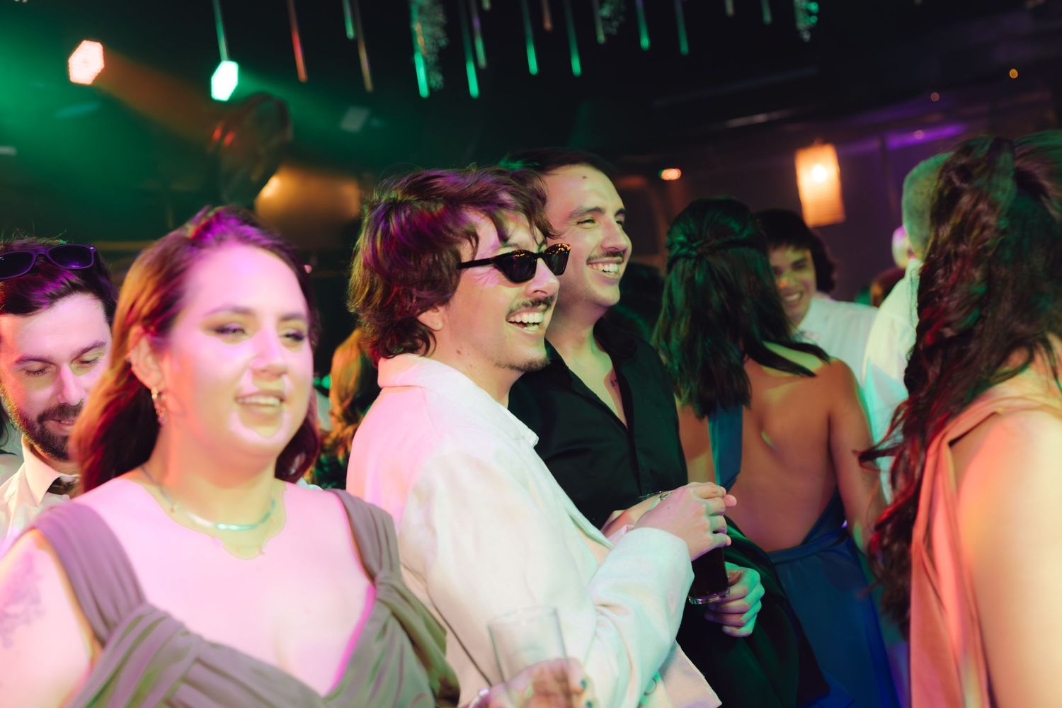 Wedding guests dance and celebrate under colorful lights at a lively reception party.