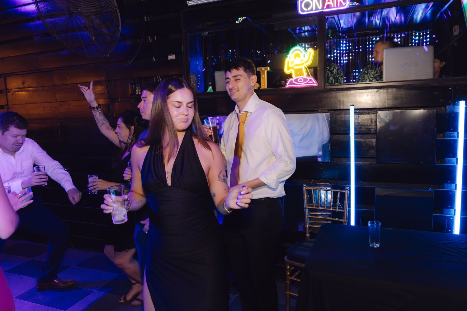 Couple dancing together at a nightclub with neon signs and blue lights in the background.