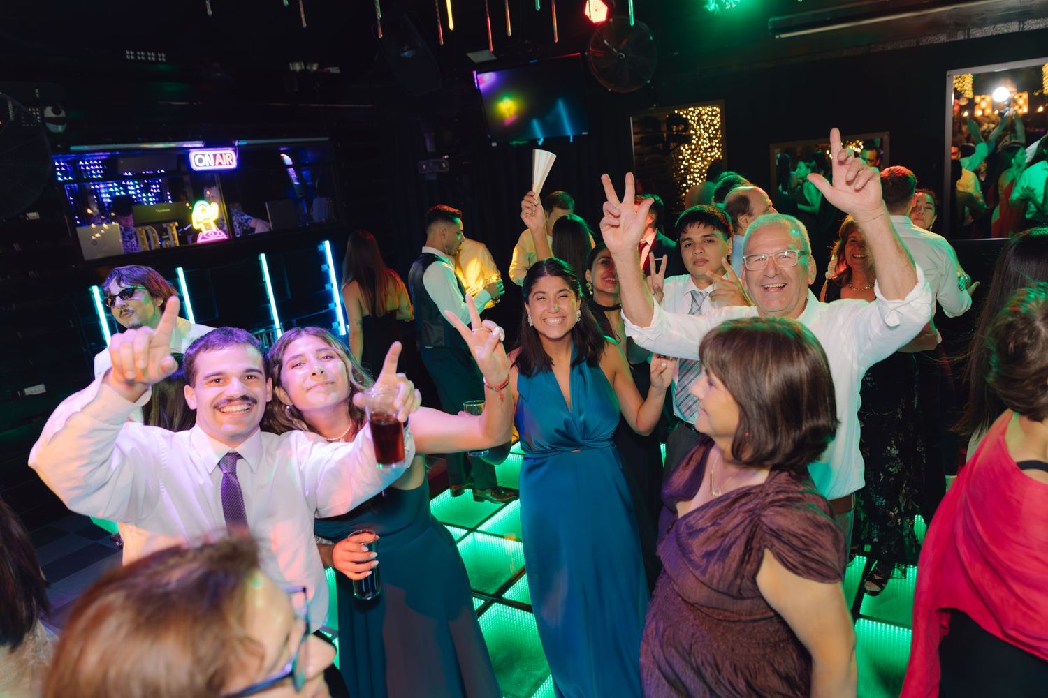 Group of joyful wedding guests posing and celebrating on a nightclub dance floor with green lights.