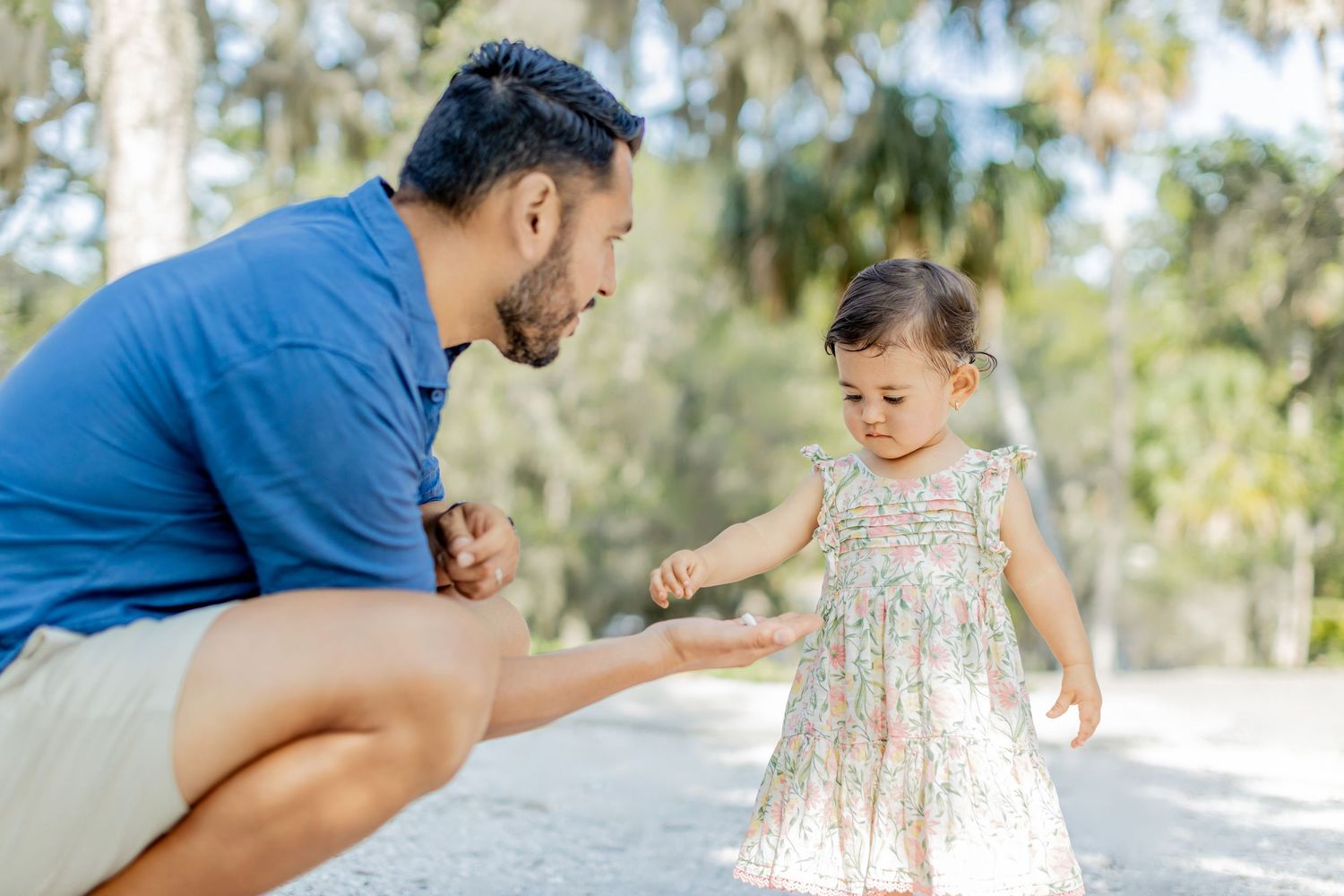 A parent and small child share sweet playful moments together on a bright sunny path surrounded by palm trees.