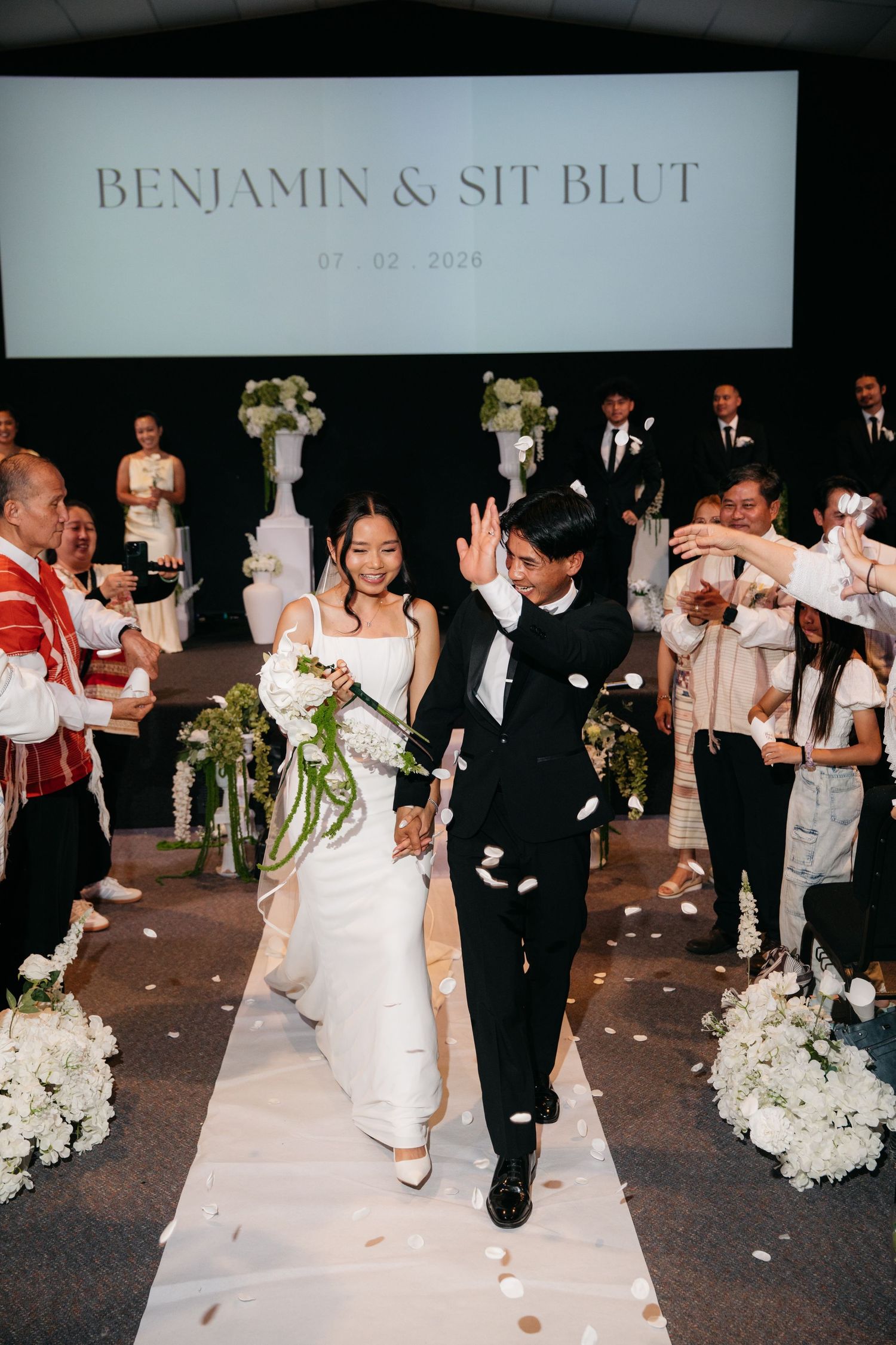 Benjamin and Sit Blut walk down the aisle as guests toss white flower petals at their elegant wedding ceremony.