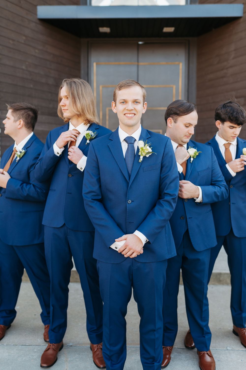 Groom and groomsmen in navy blue suits with boutonnieres pose outside wedding venue.