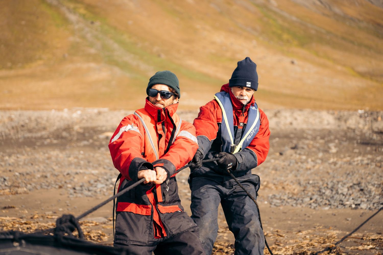 Deux membres d'équipage halant un cordage sur la plage de galets de Kapp Lee
