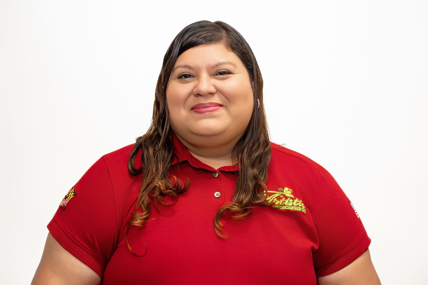 Young woman smiling in a red Artistic Landscaping polo shirt against a white background.