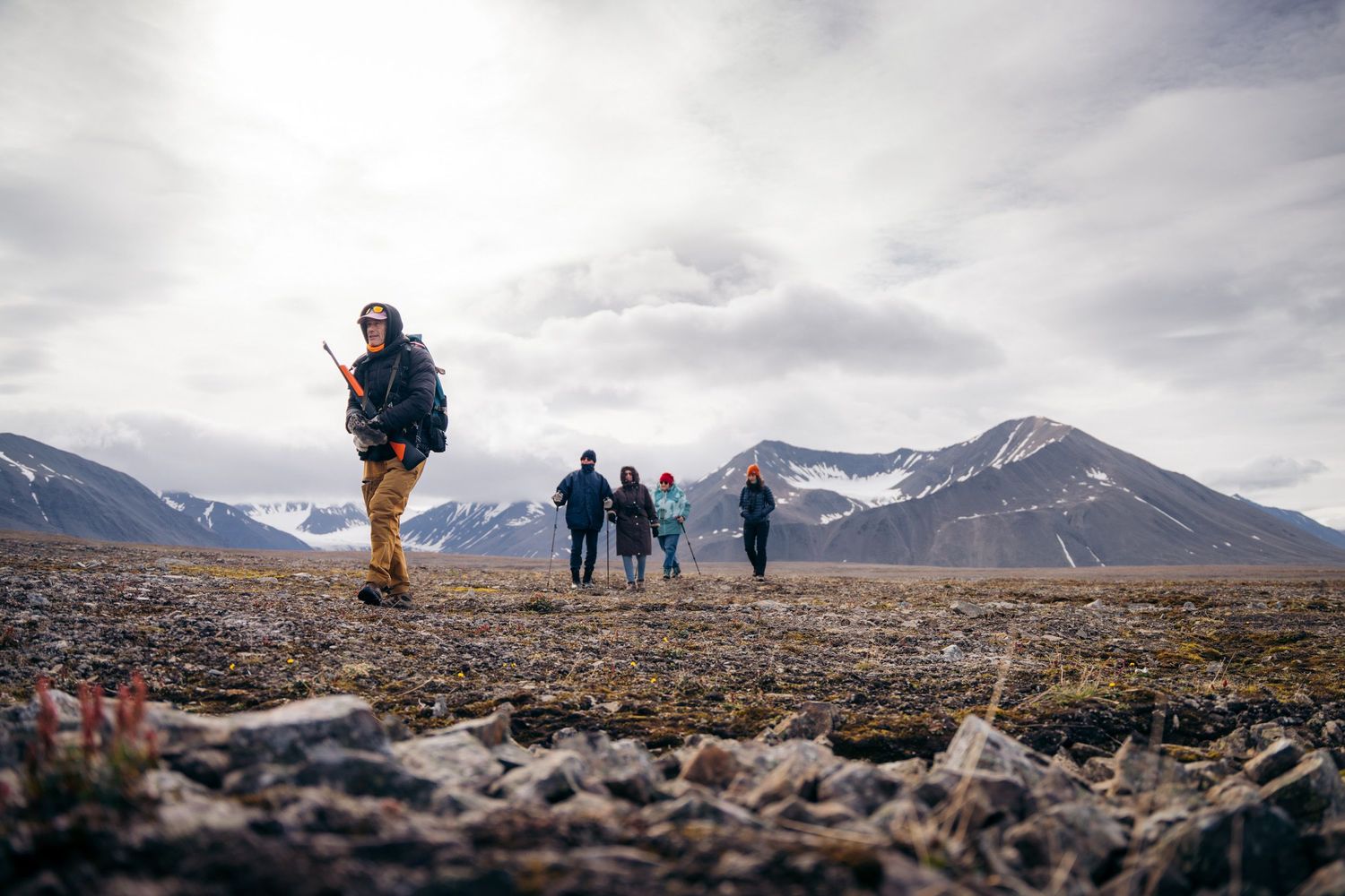 Groupe de randonneurs mené par un guide armé devant une chaîne de montagnes enneigées