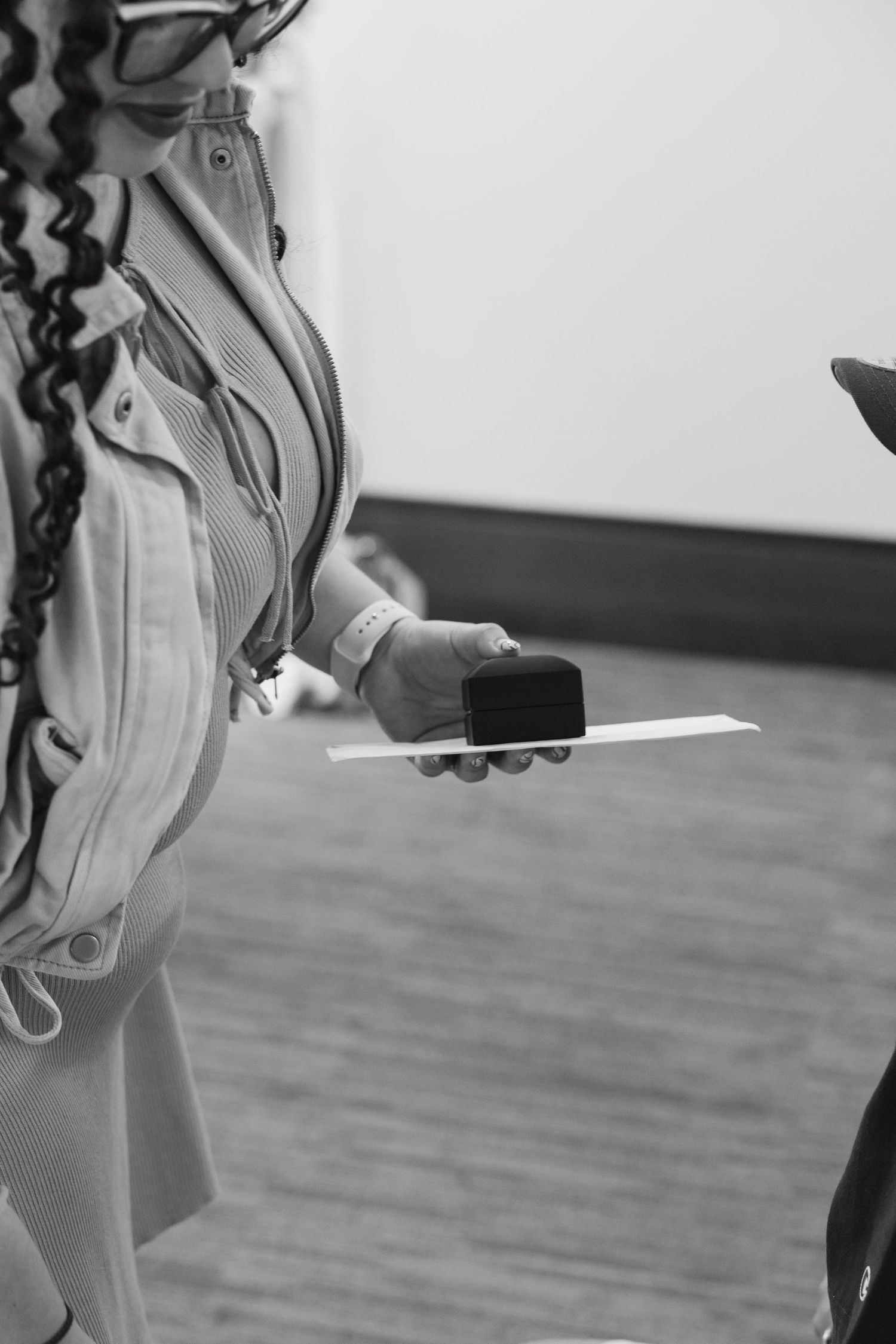 Black and white photo of a woman with curly hair holding a card reader and paper in an indoor setting.