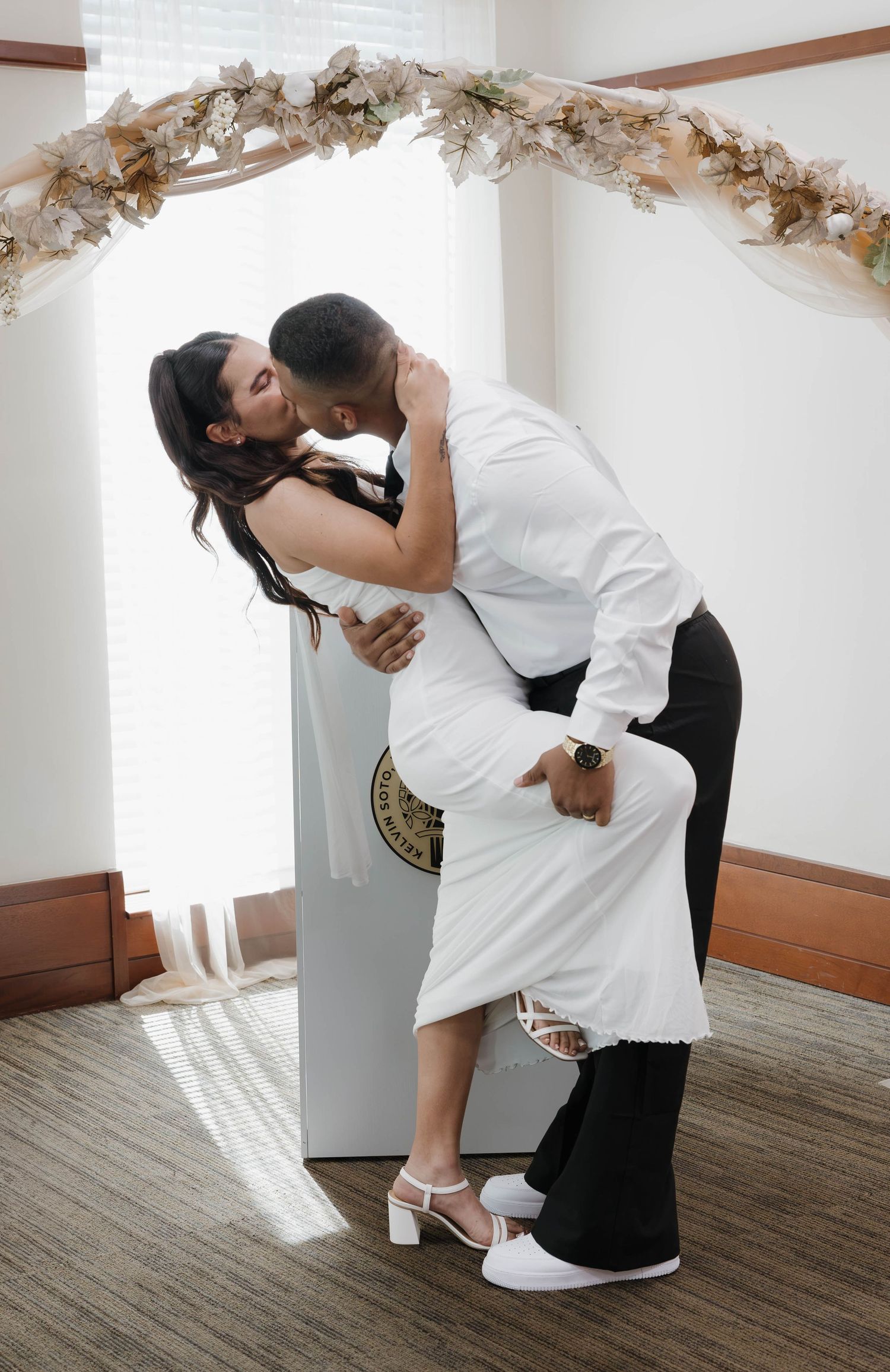 Bride and groom share a romantic dip kiss under a floral arch at their wedding ceremony.