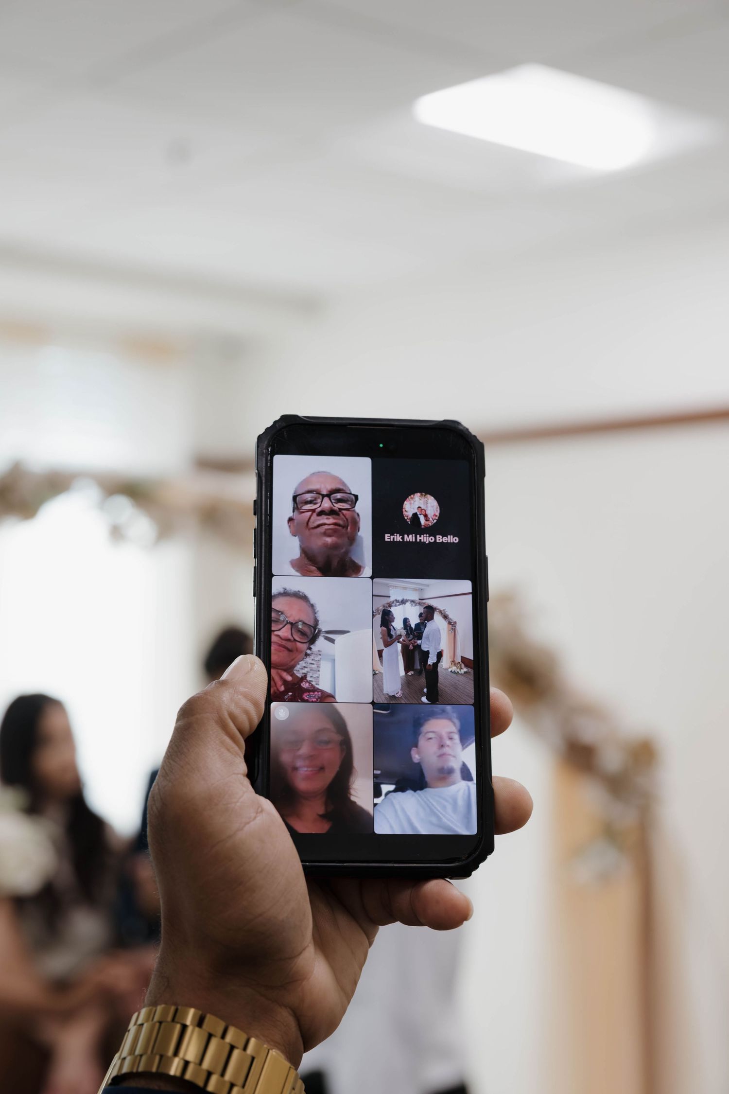 A hand holding a smartphone displaying a group video call with multiple participants on the screen.