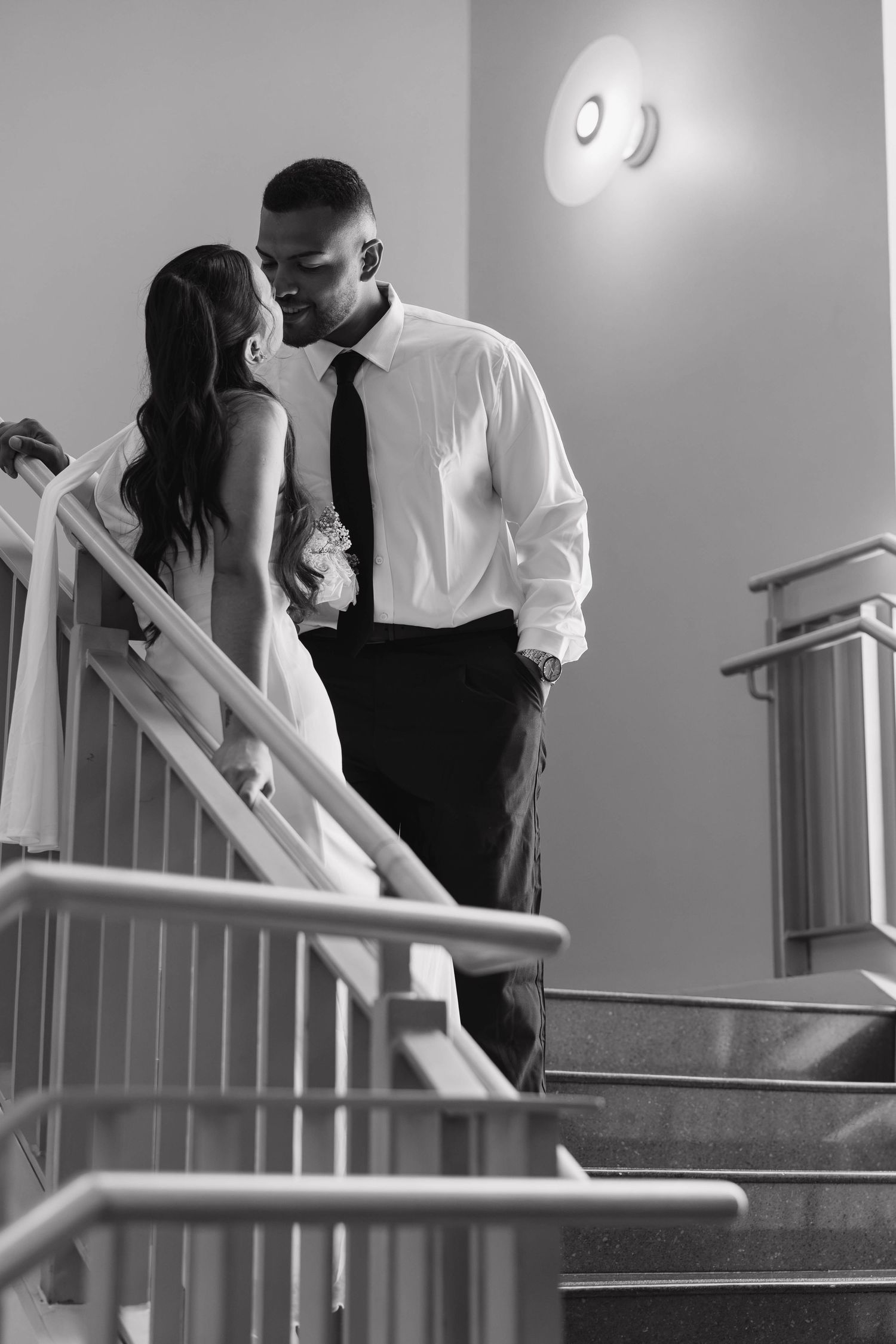 Bride and groom share a tender kiss on a staircase in a black and white wedding photo.