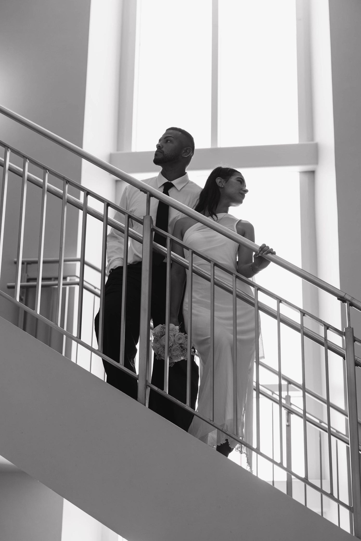 Bride and groom standing back-to-back on staircase in black and white wedding portrait.