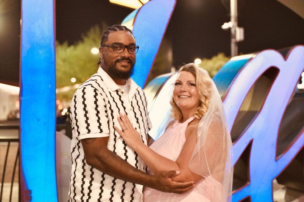 Couple posing together in front of a neon Las Vegas sign at night, woman in pink dress with veil.