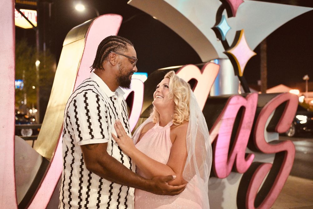 Couple sharing a romantic moment in front of a colorful Las Vegas sign at night.