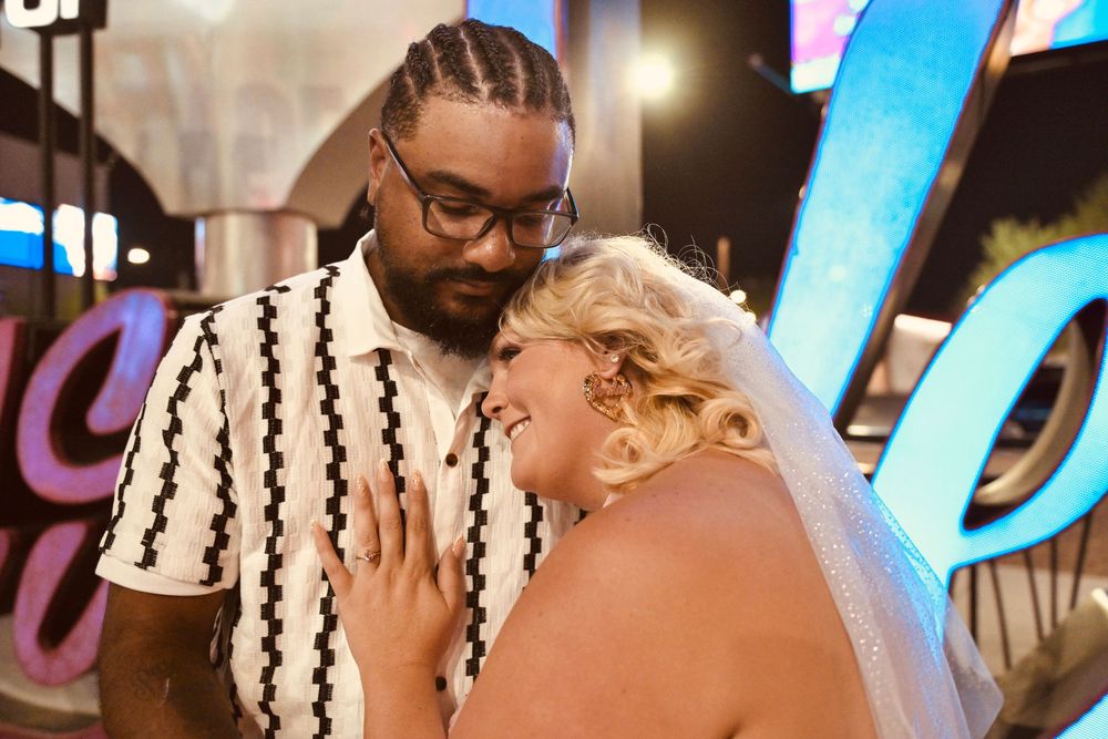 Couple sharing a romantic moment in Las Vegas, bride in veil and groom in striped shirt admiring her ring.