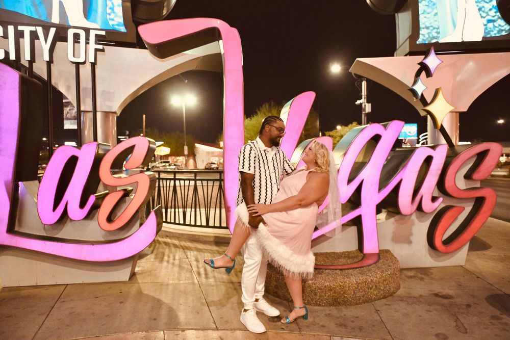 Couple posing romantically in front of the City of Las Vegas neon sign at night.