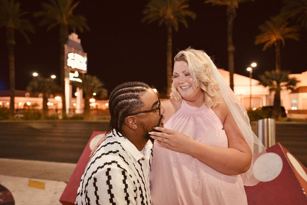 Couple sharing a romantic moment outdoors at night in Las Vegas, woman in pink dress and man in black and white outfit.