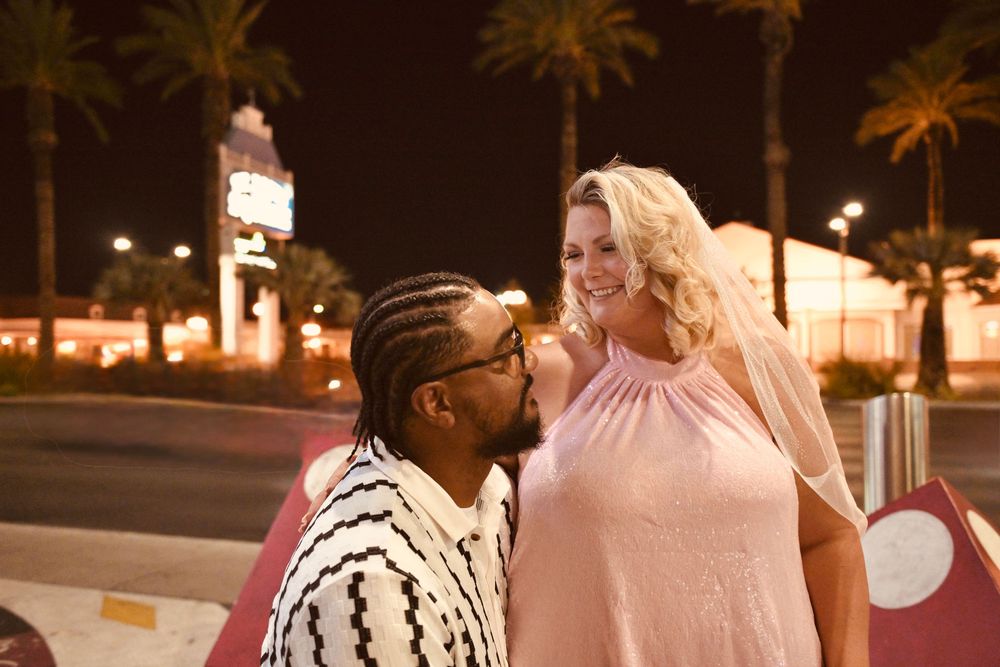Couple sharing a romantic moment outdoors at night near a lit street with palm trees in the background.