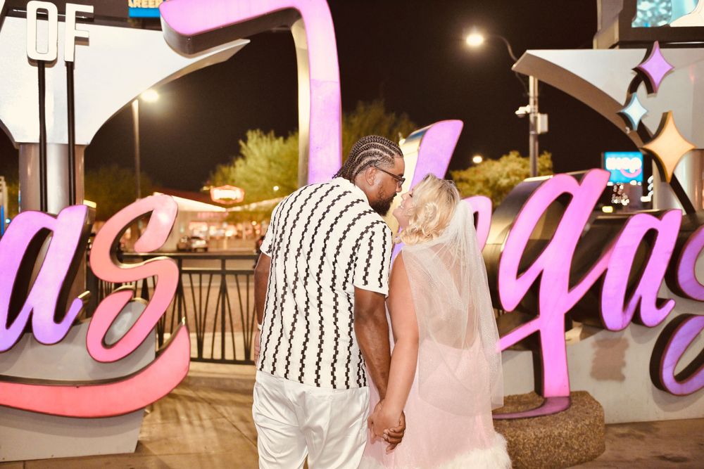 Couple holding hands in front of illuminated Las Vegas sign at night, romantic getaway.