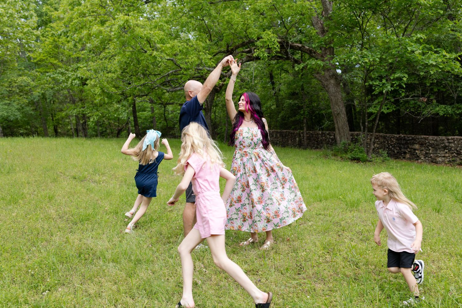 Family dancing and playing together in a lush green meadow on a sunny day outdoors.