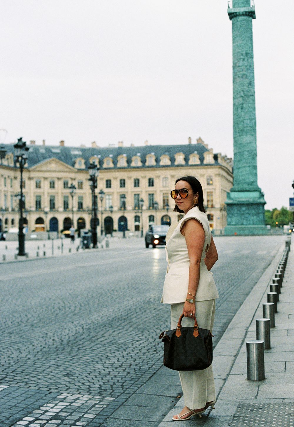 Woman in white outfit holding Louis Vuitton bag at Place Vendôme, Paris, with iconic column in background. Paris film photographer, fashion